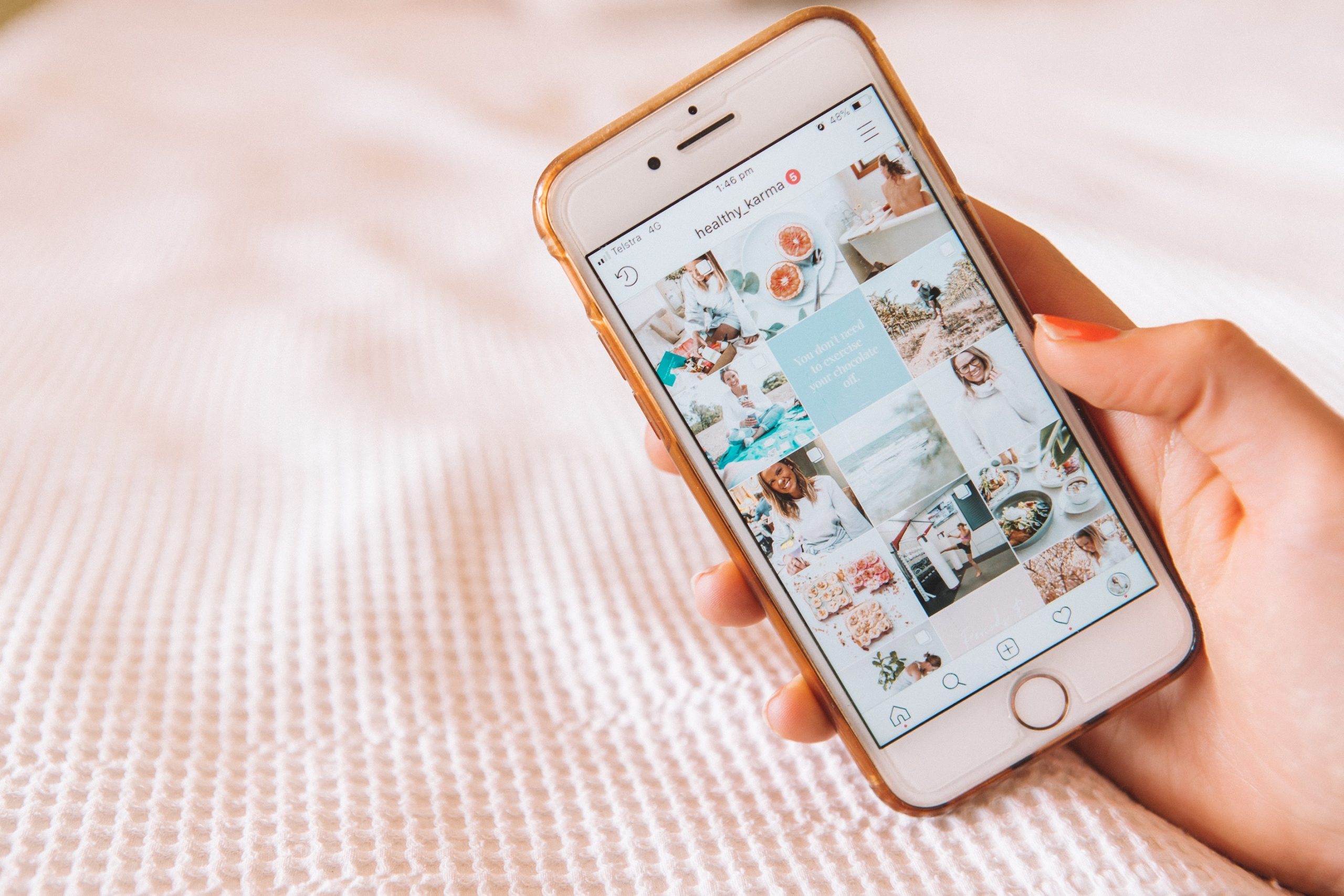 A rose gold mobile phone with the Instagram app open and a light pink bedding background